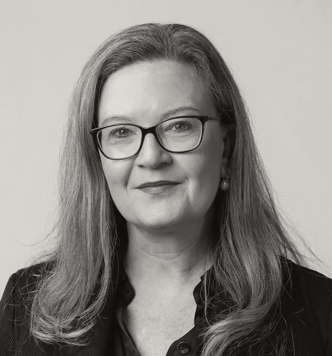 A black and white headshot of Emma McDonald. She has long hair, glasses, and is wearing a black shirt.