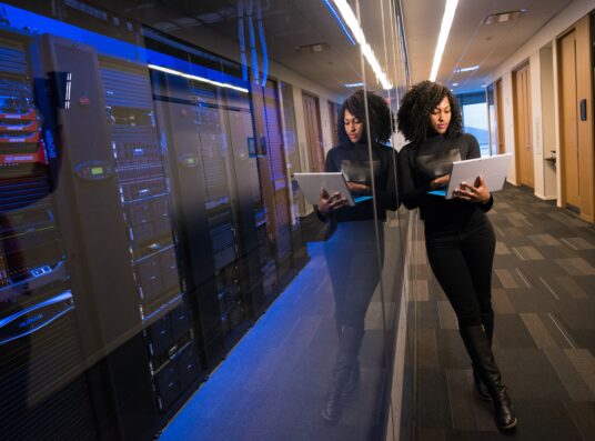 A woman with a laptop next to a server room.