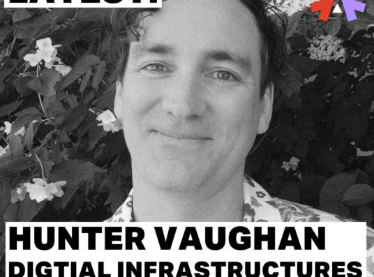 A black and and white photo of Hunter Vaughan, he has short hair with a slightly curly fringe. He is standing in front of a blossoming free, and wears a floral pattern shirt. Caption reads: Latest. Hunter Vaughan, Digital Infrastructures Dublin Blog.