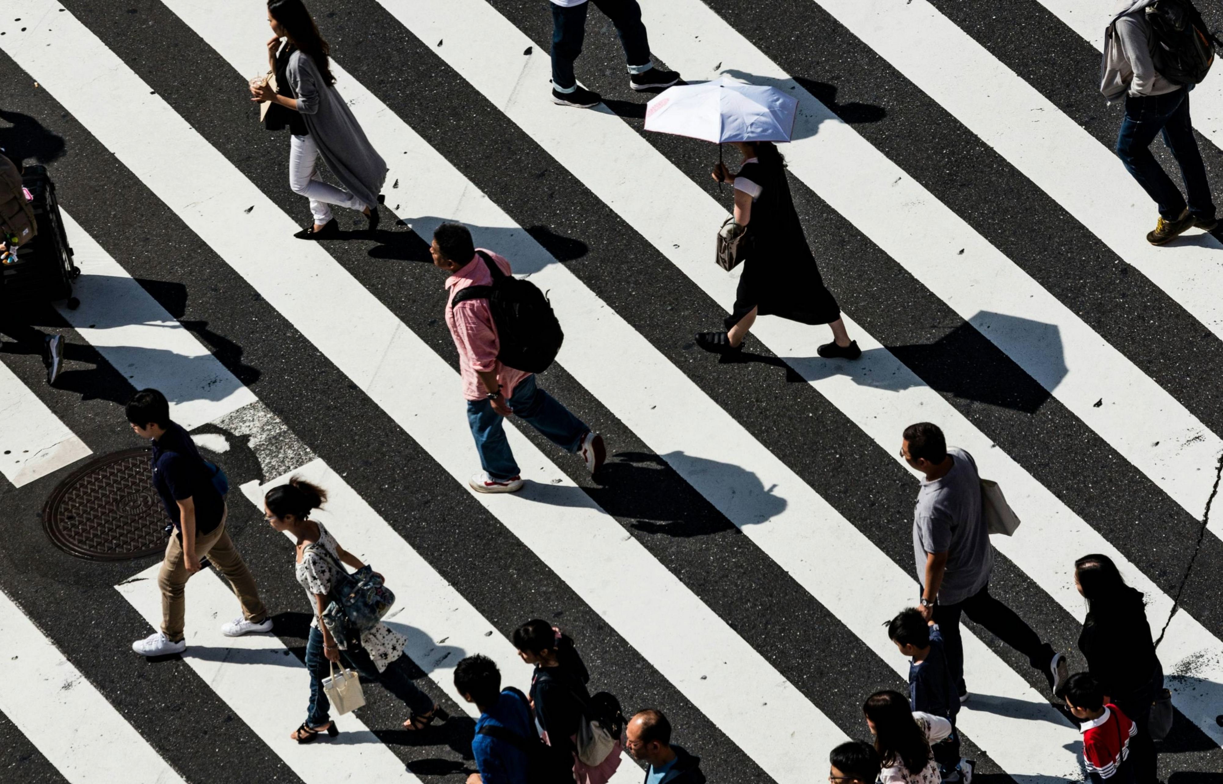A flock of pedestrians crosses a large sunlit crosswalk