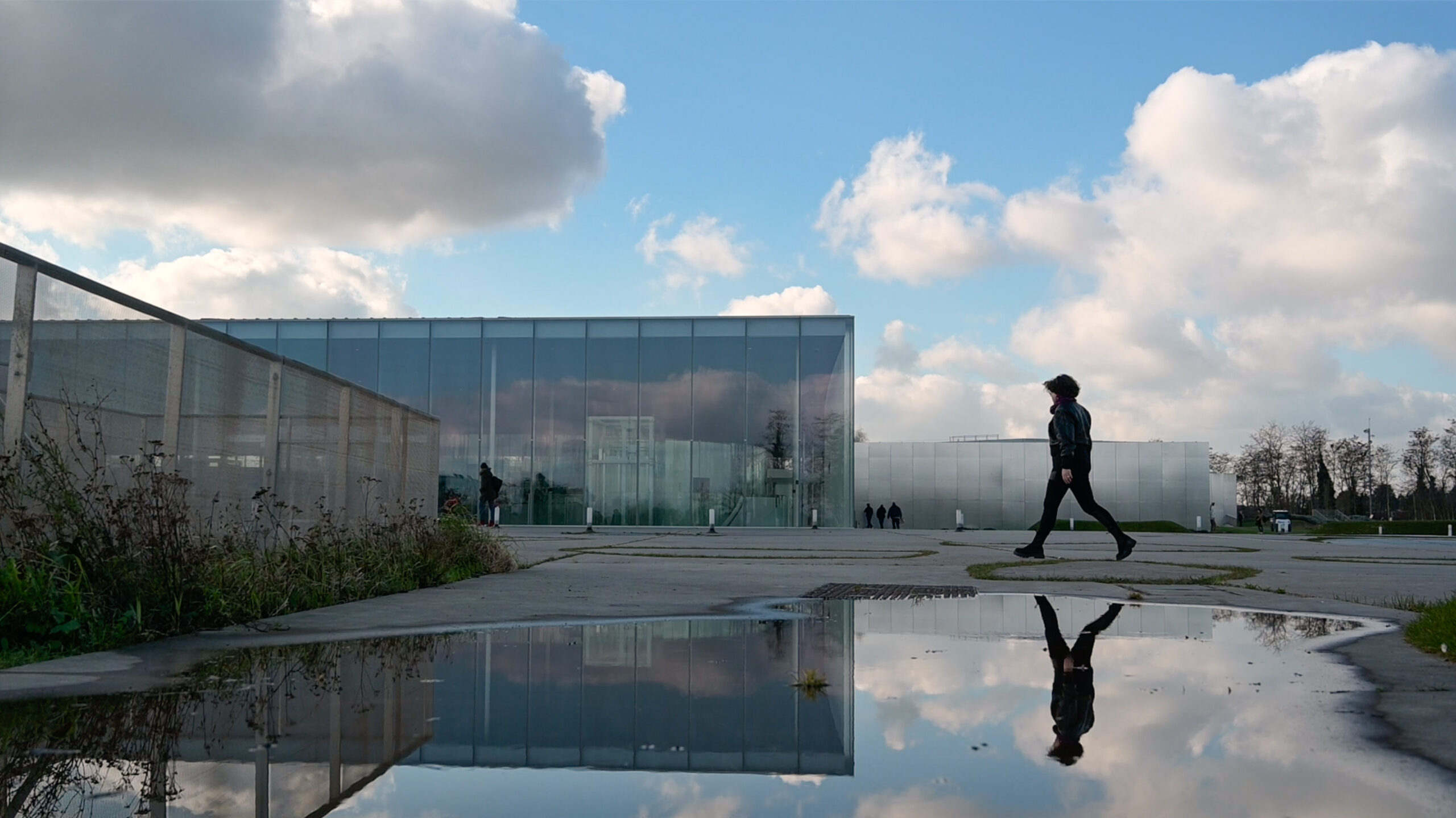 A woman crosses a courtyard, reflected in a puddle.